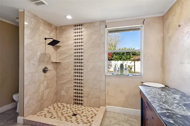 a bathroom with a granite countertop shower a toilet and a window