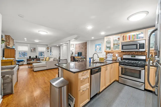 a kitchen with stainless steel appliances granite countertop a stove top oven a sink dishwasher a dining table and chairs with wooden floor