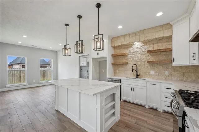 a kitchen with stainless steel appliances granite countertop a sink a stove a refrigerator and island with wooden floor