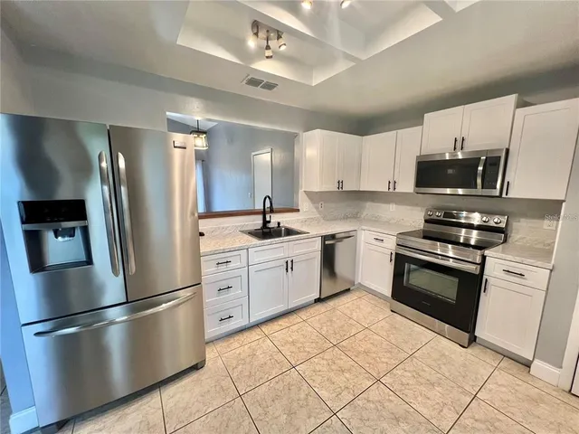 a kitchen with stainless steel appliances granite countertop a refrigerator sink and white cabinets