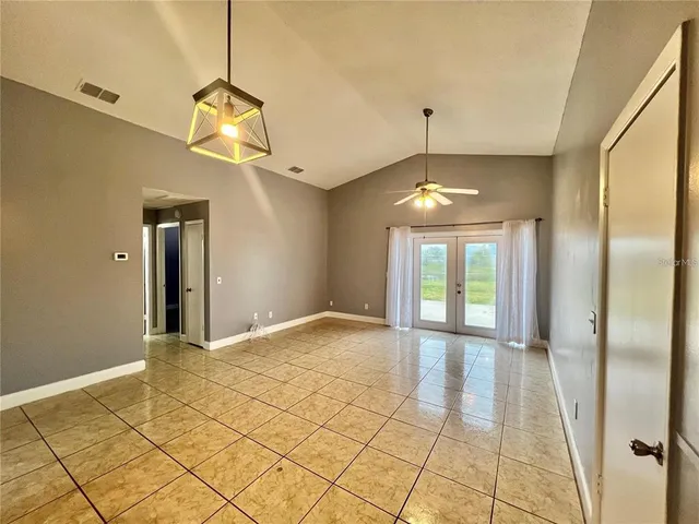 a view of an empty room with window and chandelier fan
