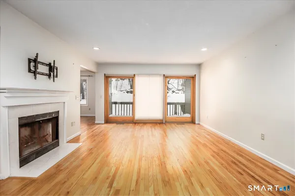 a view of an empty room with wooden floor fireplace and a window