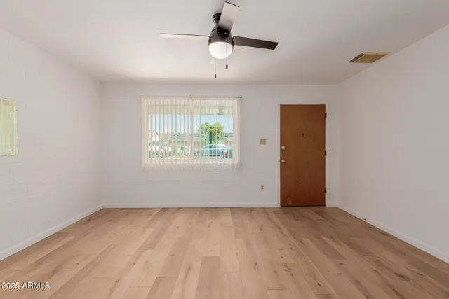 an empty room with wooden floor chandelier fan and windows
