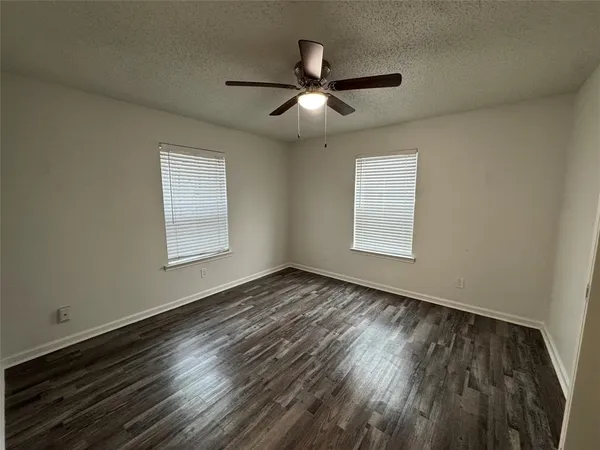 an empty room with wooden floor ceiling fan and windows