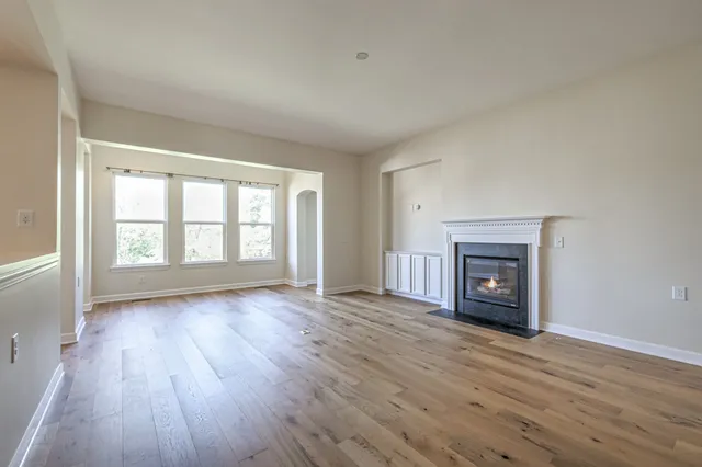 an empty room with wooden floor fireplace and windows