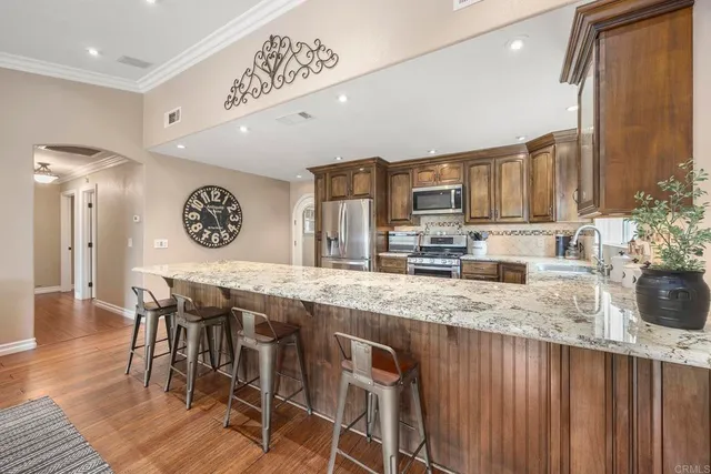 a kitchen with stainless steel appliances granite countertop a stove top oven a sink a dining table and chairs with wooden floor