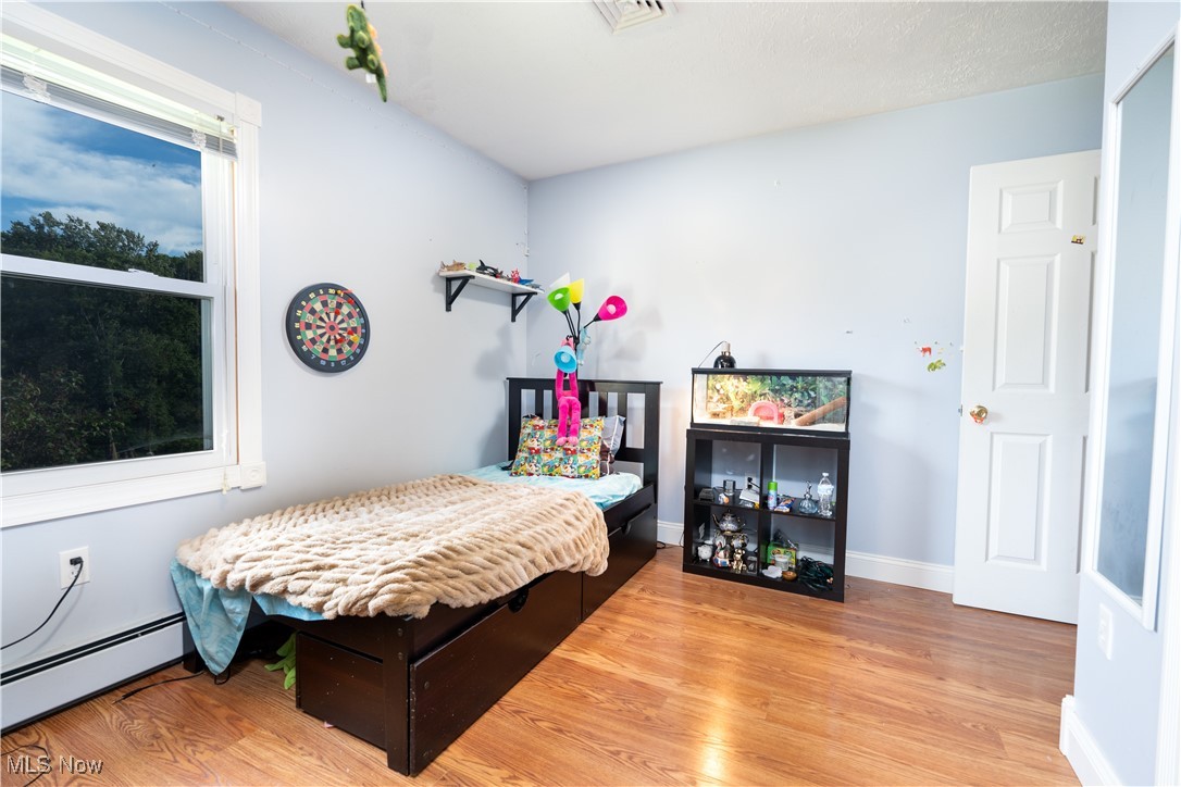 Bedroom with a baseboard heating unit and light hardwood / wood-style flooring