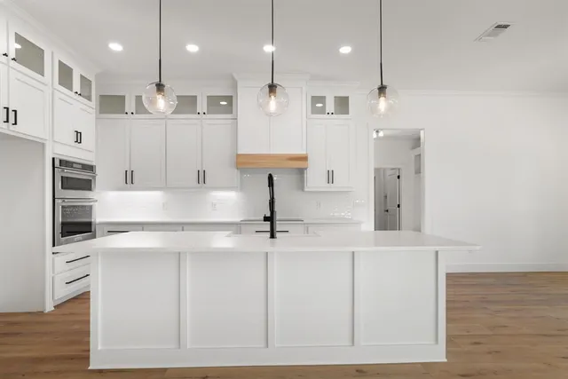 a kitchen with stainless steel appliances sink a stove and white cabinets with wooden floor