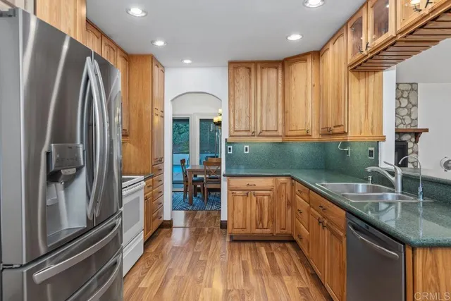 a kitchen with stainless steel appliances granite countertop a refrigerator a sink and a stove with wooden floor
