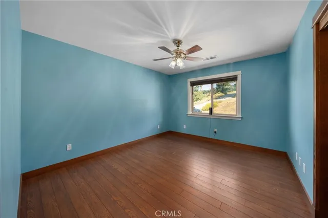 an empty room with wooden floor ceiling fan and windows