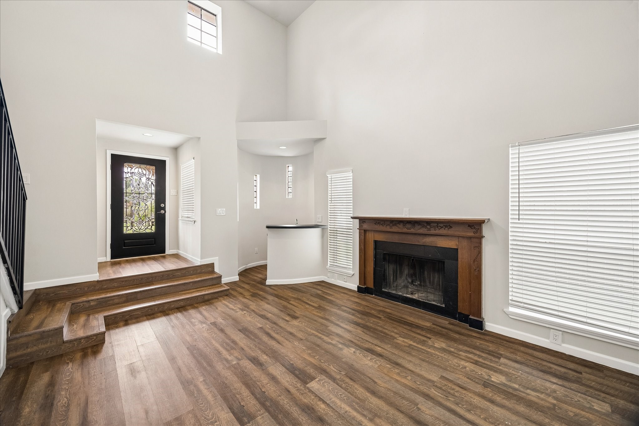 10411 Goodrum Road Houston, TX 77041 - Photo 4 of 25 Step inside and you’ll notice the spacious living room with soaring ceilings, wood-look flooring, abundant natural light, and a charming fireplace with an ornate wood mantel. The elevated entry and decorative glass front door create a stunning first impression, while the open layout offers both comfort and style.