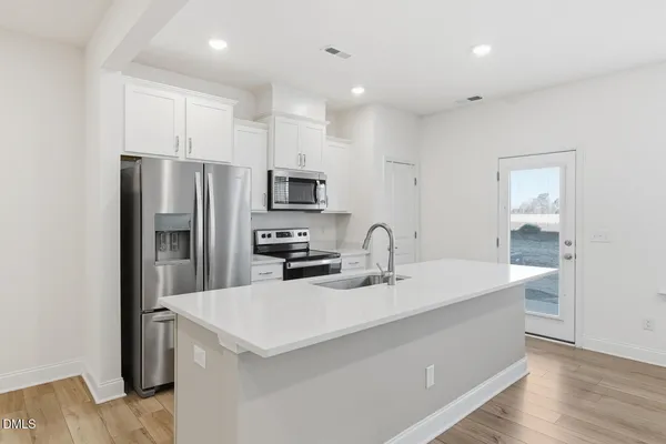 a large white kitchen with a refrigerator a sink dishwasher and a stove with wooden floor