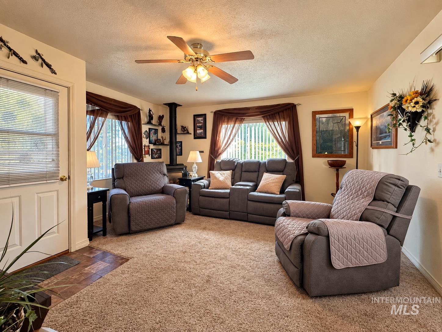 181 Hillcrest Road Burley, ID 83318 - Photo 7 of 14 Ceiling fan with integrated lighting, wood-finish flooring, wall-mounted shelving, and a prominent wood-burning stove