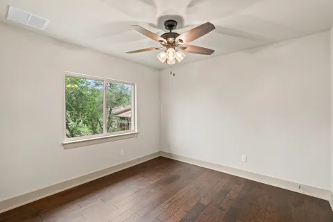an empty room with wooden floor chandelier fan and windows