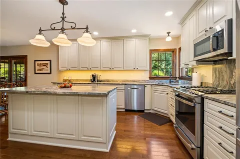 a kitchen with stainless steel appliances granite countertop a sink a stove a refrigerator cabinets and a window