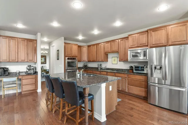 a kitchen with stainless steel appliances granite countertop a refrigerator a stove top oven a sink dishwasher and white cabinets with wooden floor