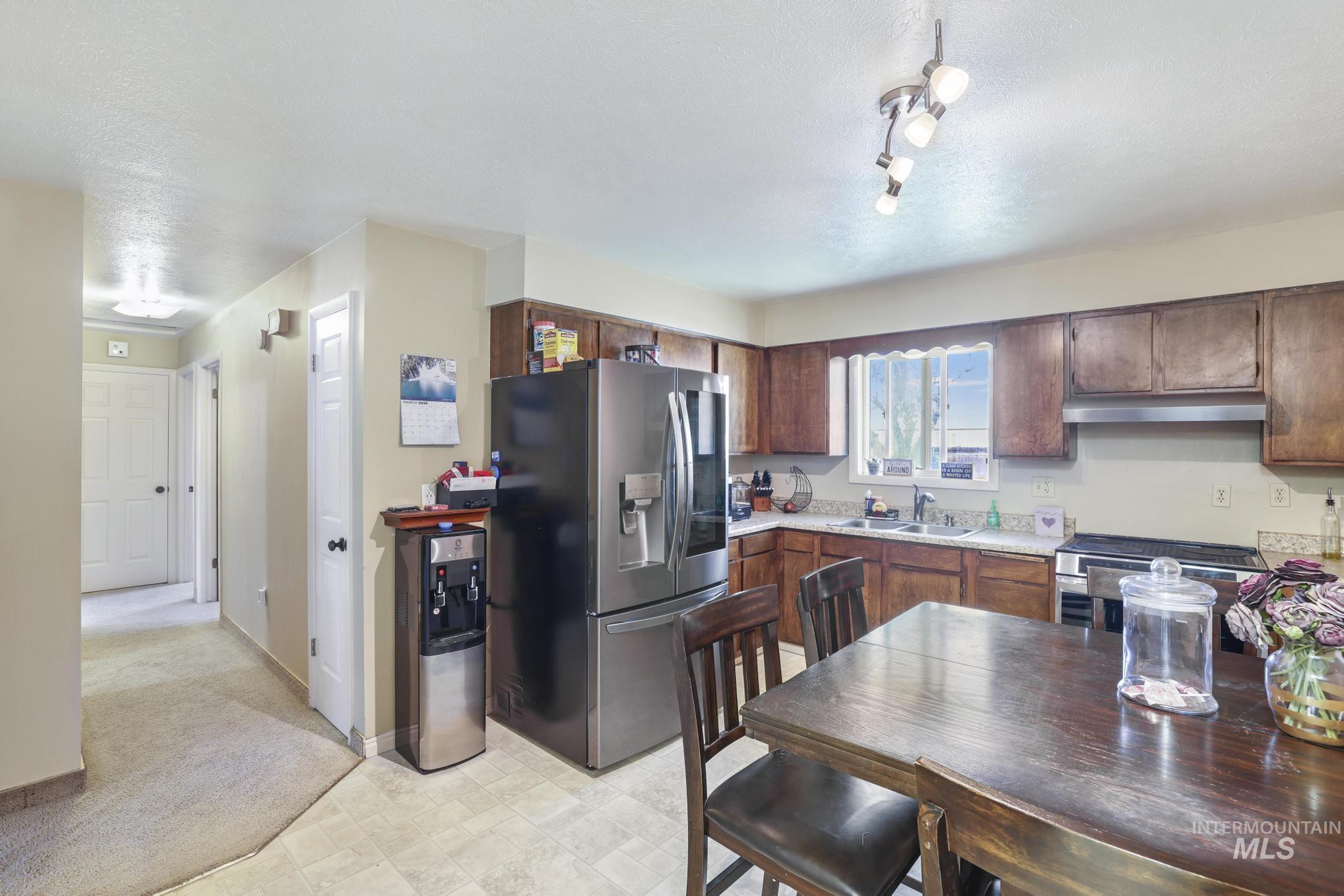 618 Sharon Street Rupert, ID 83350 - Photo 7 of 20 Kitchen featuring stainless steel appliances, light countertops, a textured ceiling, dark wood finish cabinetry, and light carpet
