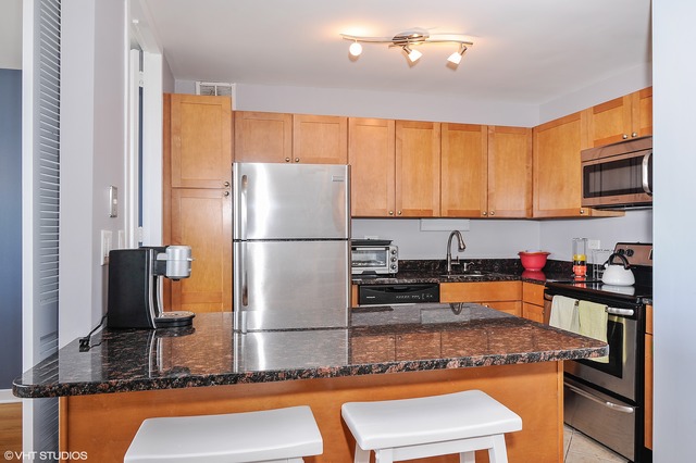655 West Irving Park Road, Unit 3506 Chicago, IL 60613 - Photo 4 of 9 a kitchen with stainless steel appliances granite countertop a refrigerator a stove and a sink with wooden cabinets