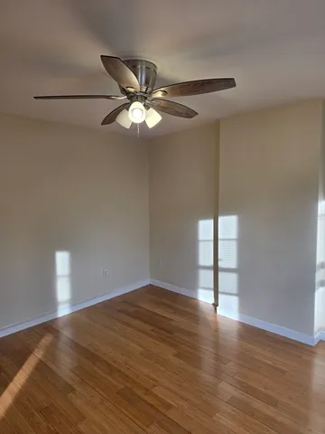 a view of an empty room with wooden floor and a ceiling fan