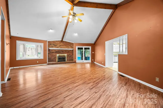 a view of an empty room with wooden floor fireplace and a window
