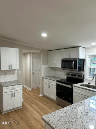 a kitchen with stainless steel appliances granite countertop a stove top oven a sink dishwasher and a microwave oven with white cabinets