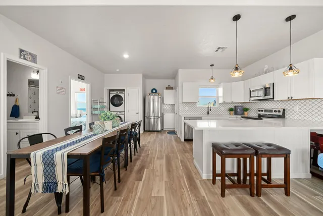 a open kitchen with stainless steel appliances granite countertop a stove top oven a sink a dining table and chairs with wooden floor