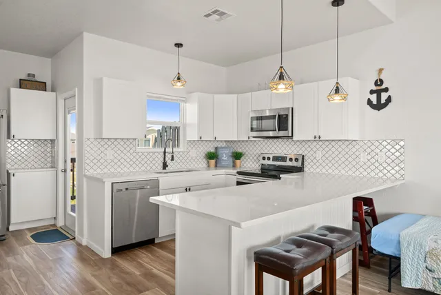 a kitchen with stainless steel appliances a stove a sink a refrigerator a center island a stove and a refrigerator with wooden floor