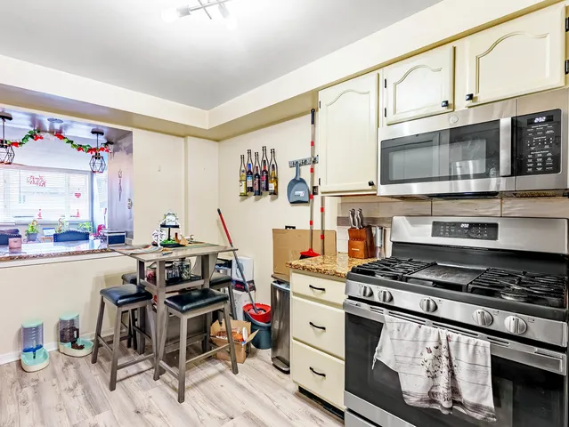 a kitchen with stainless steel appliances kitchen island granite countertop a stove top oven a sink a dining table and chairs with wooden floor