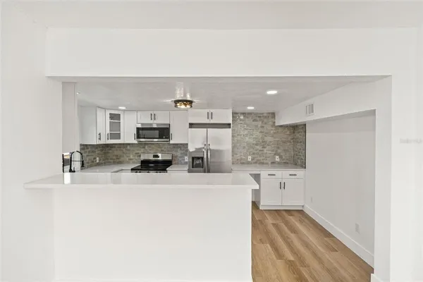 a kitchen with stainless steel appliances granite countertop a refrigerator a stove oven and white cabinets with wooden floors