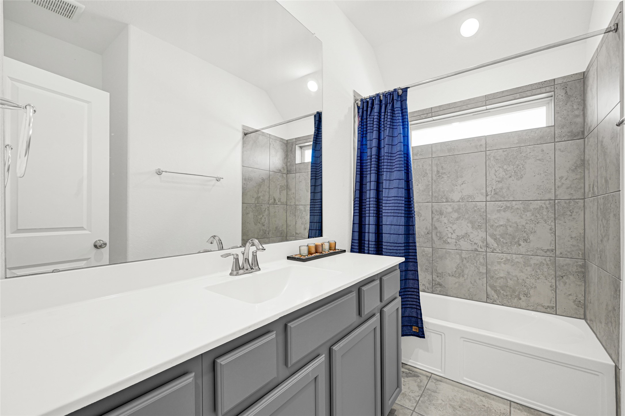 4307 Annandale Lane Rosharon, TX 77583 - Photo 20 of 31 This additional second floor bathroom features a modern design with a sleek white countertop, gray cabinetry, and a tiled shower area complemented by a blue curtain. It has ample natural light and a spacious mirror, also offering a clean and contemporary feel.