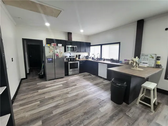 a kitchen with stainless steel appliances granite countertop a refrigerator a sink dishwasher a stove and a dining table with wooden floor