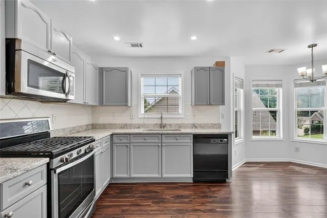 a kitchen with stainless steel appliances granite countertop a stove top oven a sink dishwasher and a microwave oven with wooden floor