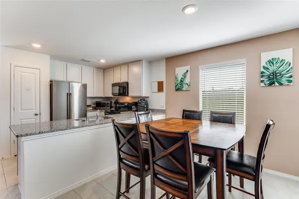 a kitchen with stainless steel appliances granite countertop a dining table chairs and refrigerator
