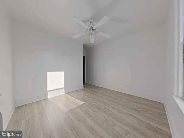 a view of an empty room with wooden floor and a ceiling fan