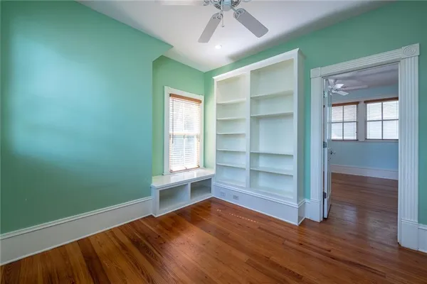 a view of an empty room with wooden floor and a ceiling fan