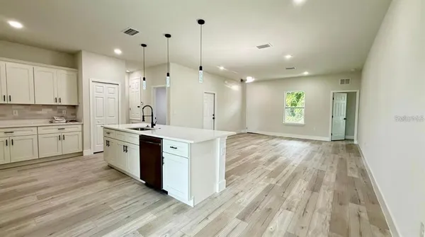 a kitchen with stainless steel appliances kitchen island granite countertop a refrigerator a sink dishwasher a stove and white cabinets with wooden floor