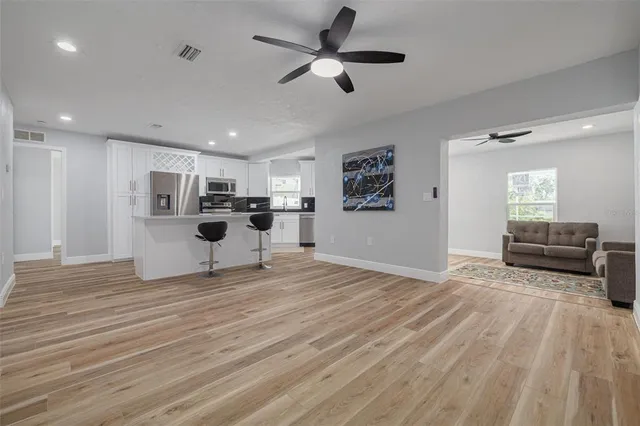 a view of a livingroom with kitchen island stainless steel appliances refrigerator stove and wooden floor