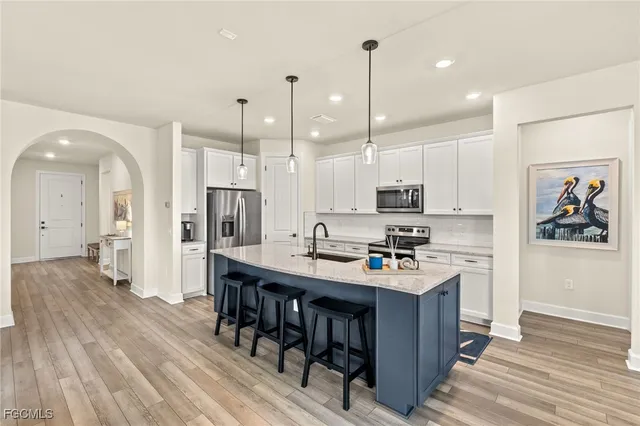 a kitchen with stainless steel appliances granite countertop a stove top oven a refrigerator a sink and white cabinets with wooden floor