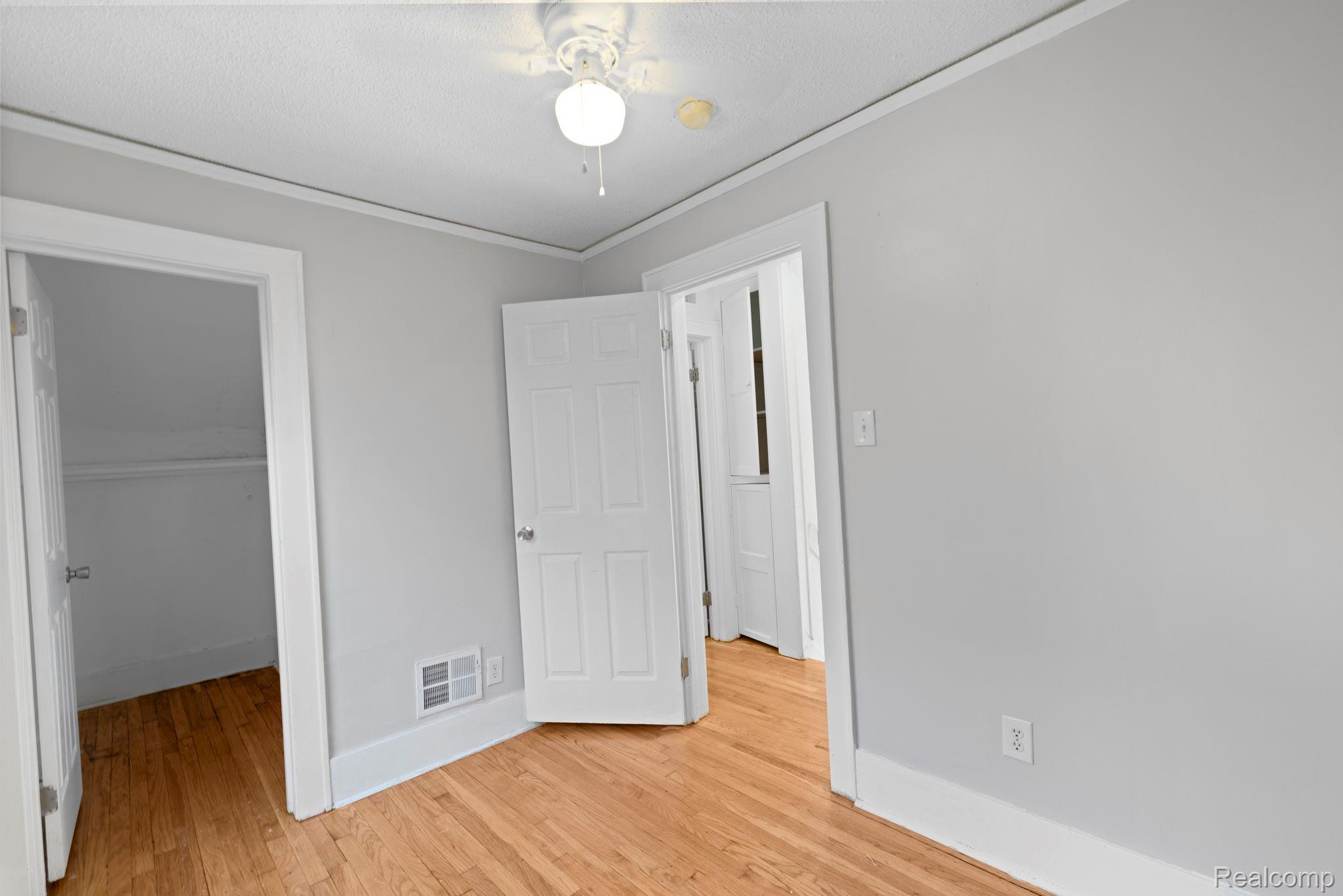 74 Pine Street River Rouge, MI 48218 - Photo 19 of 28 Unfurnished bedroom featuring a walk in closet, ornamental molding, light wood-type flooring, and ceiling fan