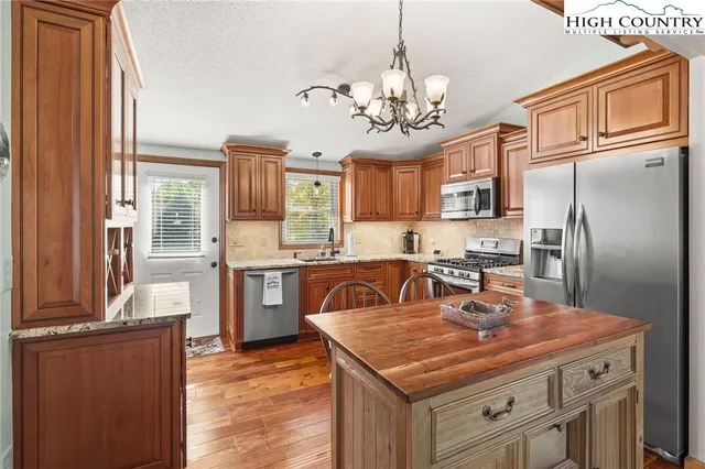 a kitchen with stainless steel appliances granite countertop a refrigerator a sink dishwasher a stove and a dining table with wooden floor