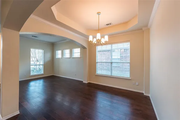 an empty room with wooden floor chandelier and windows