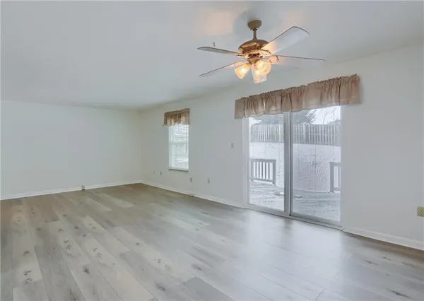 an empty room with wooden floor chandelier fan and windows