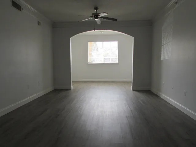 an empty room with wooden floor chandelier fan and windows