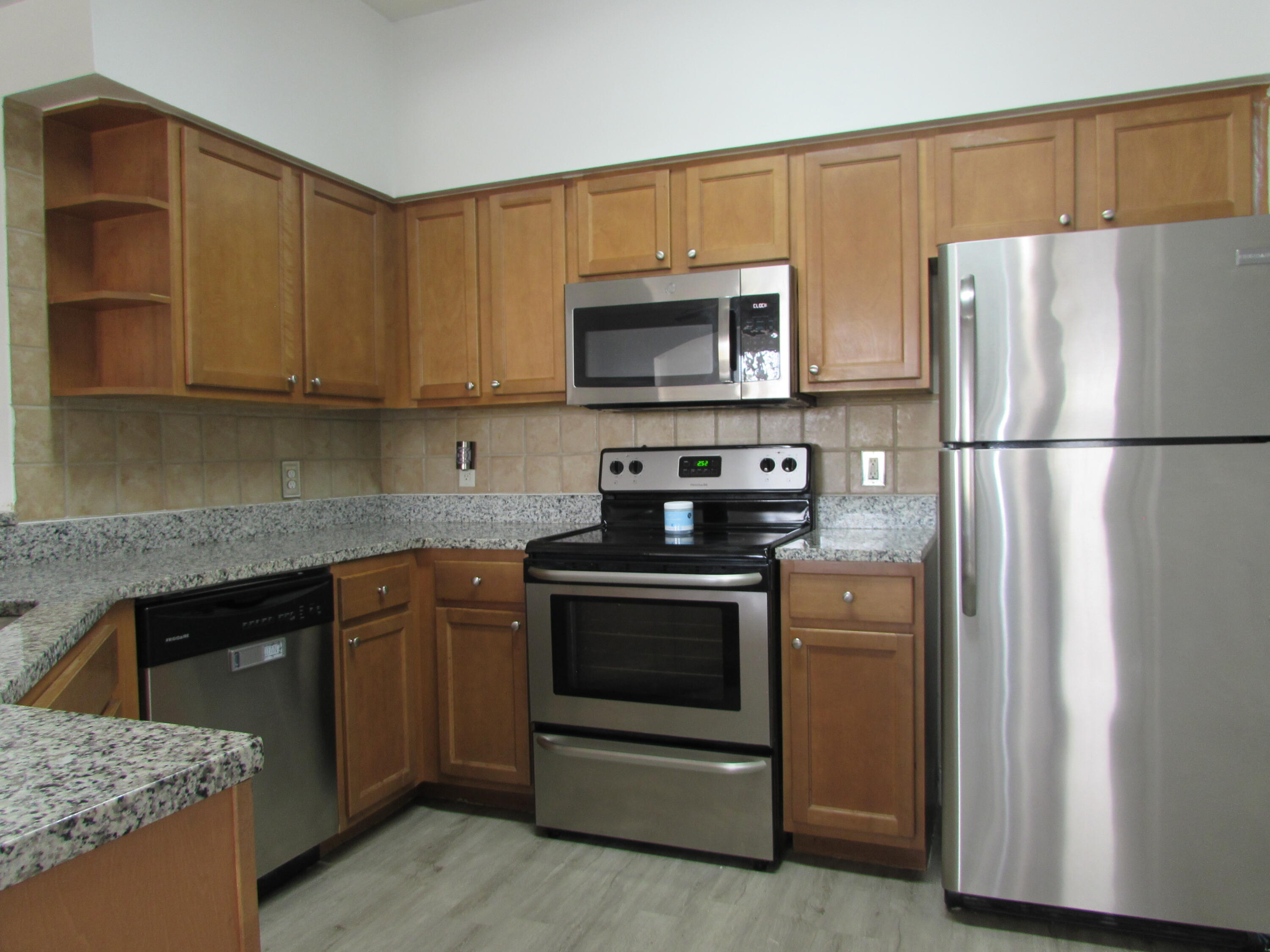 9873 Baywinds Boulevard, Unit 5107 West Palm Beach, FL 33411 - Photo 3 of 22 a kitchen with stainless steel appliances granite countertop a refrigerator stove a sink and a microwave