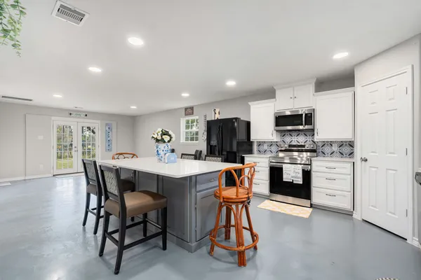 a open kitchen with stainless steel appliances kitchen island granite countertop a dining table chairs and refrigerator