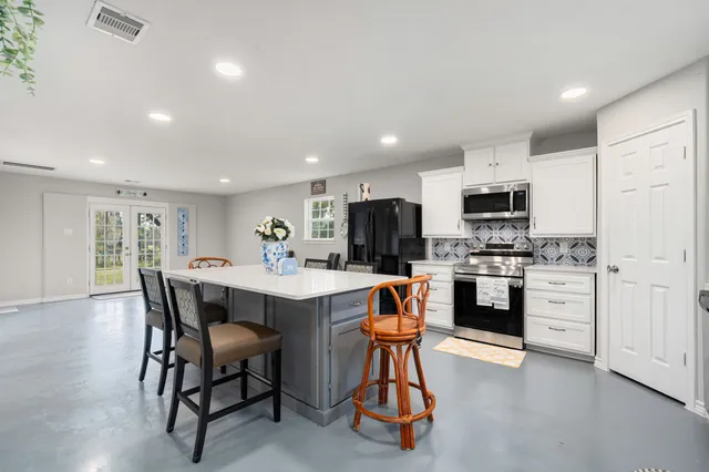 a open kitchen with stainless steel appliances kitchen island granite countertop a dining table chairs and refrigerator