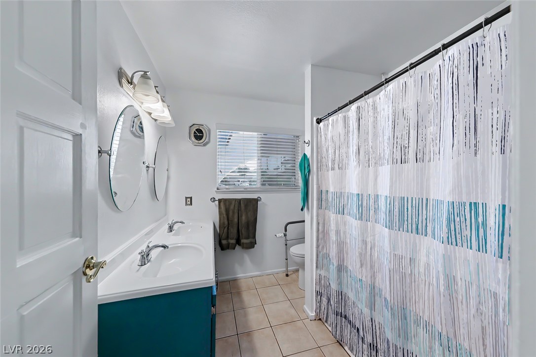 3107 Trueno Road Henderson, NV 89014 - Photo 28 of 37 A well-lit bathroom provides dual sinks and a shower with patterned curtain.