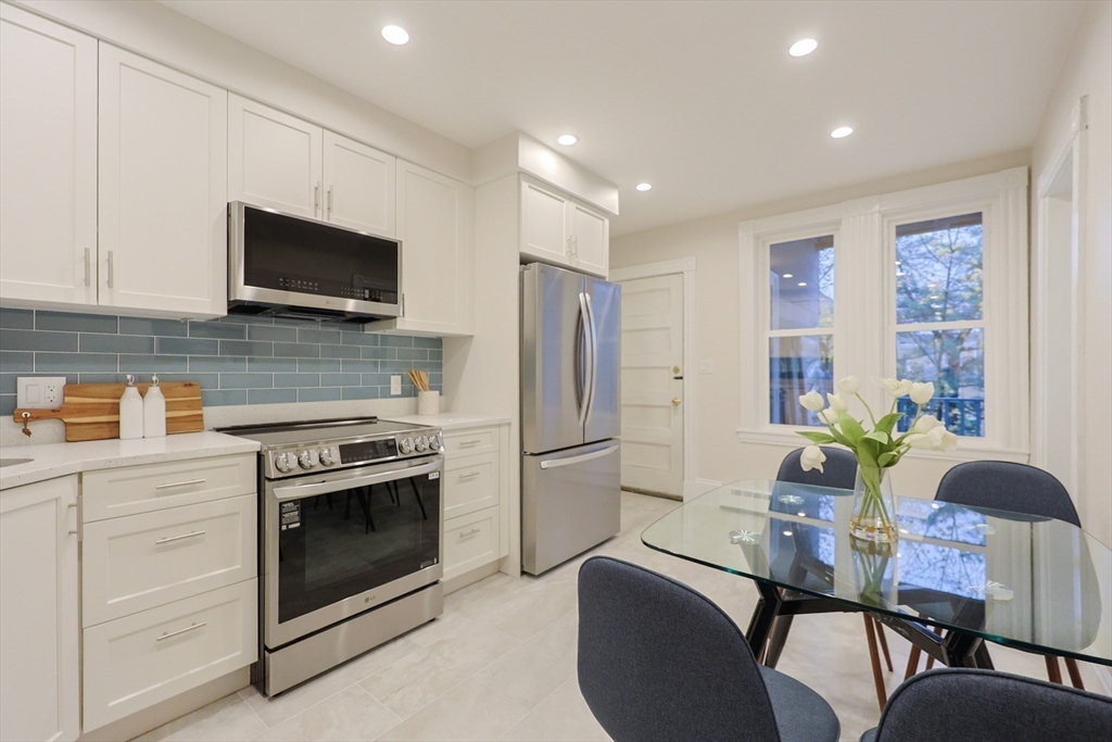 28 Inman Street, Unit 4 Cambridge, MA 02139 - Photo 7 of 32 a kitchen with stainless steel appliances a stove a refrigerator a microwave a dining table and chairs with wooden floor