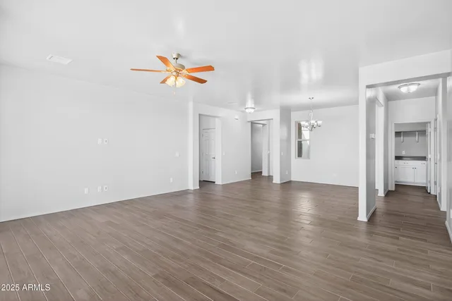 a view of an empty room and kitchen with wooden floor