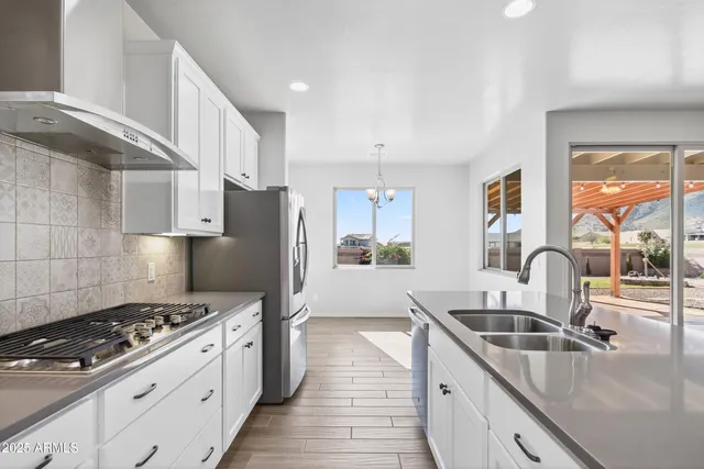 a kitchen with stainless steel appliances granite countertop a refrigerator a stove and white cabinets with wooden floor